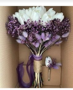 a bouquet of flowers in a cardboard box with purple ribbon and ribbons on the side