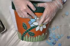 a person in white gloves painting a pot with flowers and leaves on the outside side