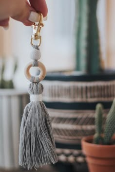 a person holding a keychain with tassels on it and a cactus in the background