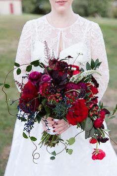 a woman in a white dress holding a bouquet of red and purple flowers on her wedding day