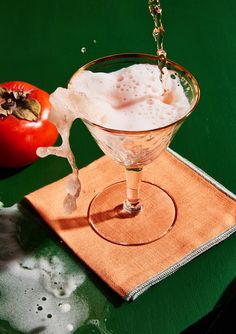 a glass filled with liquid sitting on top of a table next to an apple and tomato