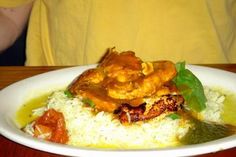 a white plate topped with rice and meat covered in sauce on top of a wooden table