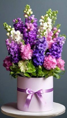 purple and white flowers are in a pink hat with a bow on the top of it