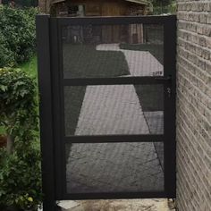 an open black gate in front of a brick wall with grass and bushes behind it