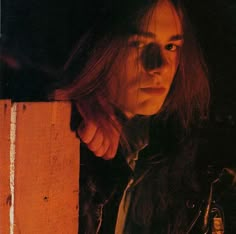 a man with long hair standing next to a wooden wall