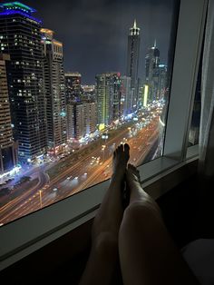 a person's feet are propped up against a window overlooking a city at night