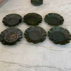 six green plates sitting on top of a white counter next to a vase with flowers in it