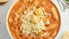 a white bowl filled with pasta and meat soup next to some bread on the side