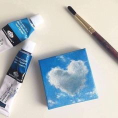 two paints and a brush sitting next to each other on a white surface with a heart shaped cloud painted on it