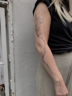 a woman with a flower tattoo on her arm standing next to a white wall and looking at the camera