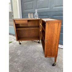 an old fashioned wooden cabinet with wheels and glass bottles on the top shelf, in front of a garage door