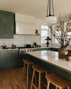 a kitchen with green cabinets and wooden stools in front of the island countertop