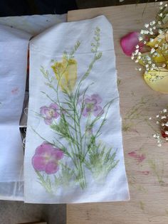 two napkins with flowers painted on them sitting on a table next to a potted plant