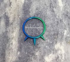 a blue and green ring with two spikes on it sitting on a stone surface next to the words omdbbakagens