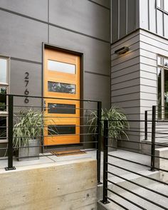 an orange door is on the side of a gray building with black railings and planters