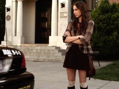 a woman standing on the sidewalk in front of a building with her arms crossed and looking off to the side