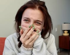 a woman covers her mouth with both hands while sitting on a couch in the living room