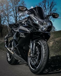 a black motorcycle parked on the side of a road next to some grass and trees