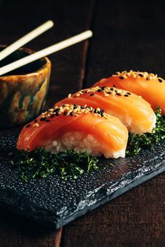 three pieces of sushi on a black plate with chopsticks next to it