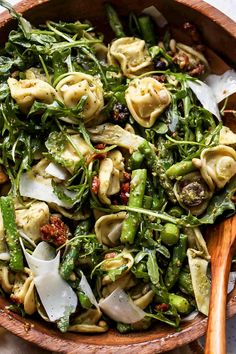 a wooden bowl filled with pasta and veggies on top of a white table