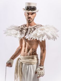 a man with tattoos and wings on his chest wearing a white hat, gloves and chains