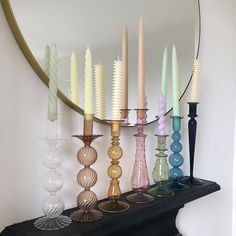 many different colored candles are lined up on a mantle with a mirror in the background