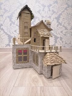 a paper model of a house made out of cardboard on a wooden floor with a damask wall in the background