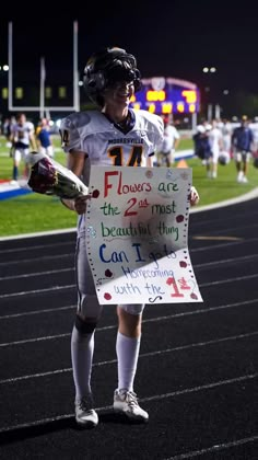 a young man holding a sign on top of a football field at night with other people in the background