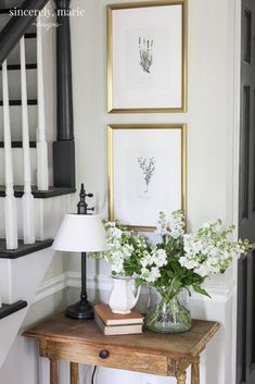 some flowers are sitting on a table in front of two framed pictures and a lamp