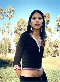 a woman standing in the grass with her hands on her hips and looking at the camera