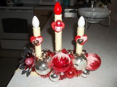 three red and white candles on top of a table next to silver balls, ornaments and tinsel