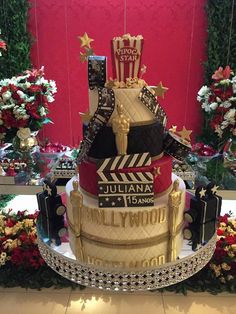 a three tiered cake is decorated with hollywood memorabilia and flowers on the table in front of a red wall