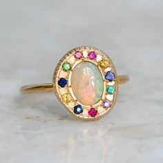 A yellow gold ring with a bezel-set oval opal centre stone, surrounded by a multicoloured halo of sapphires, a ruby and tsavorite garnets. Pebble Ring, Rainbow Opal, Tsavorite Garnet, Crystal Opal, Trendy Earrings, Precious Gems, Opal Crystal, Perfectly Imperfect, Dream Jewelry