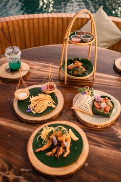 several plates with food on them sitting on a wooden table near the water at night