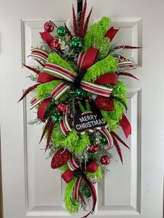 a christmas wreath hanging on a door with green and red ribbons, ornaments and decorations