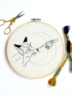 an embroidery project with scissors and thread on the table next to it is a drawing of a fox