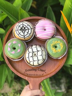 a person holding a wooden paddle with four donuts on it and spider web designs