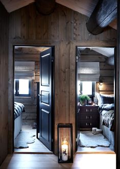 a bedroom with wooden walls and flooring has two mirrors on the wall, one door open to reveal another room