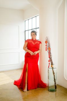 a woman in a red dress leaning against a wall next to a vase with flowers