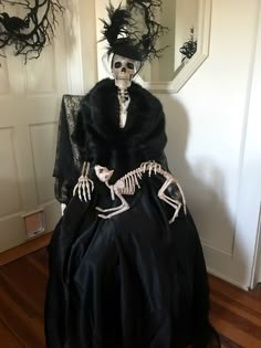 a skeleton dressed up in a black dress and hat sitting on top of a chair