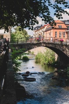 a bridge over a small river with people walking on the other side and buildings in the background