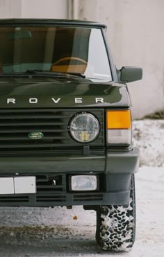 the front end of a green land rover parked on a snow covered road with its hood up