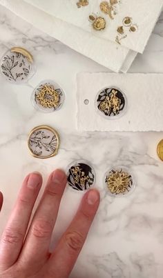 a person's hand next to some gold and black buttons on a marble surface