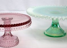 two glass dishes sitting on top of a table next to each other, one is green and the other is pink