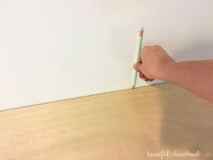 a person holding a green pen on top of a wooden table next to a white wall