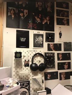 a wall covered in posters and headphones next to a computer desk with other items on it