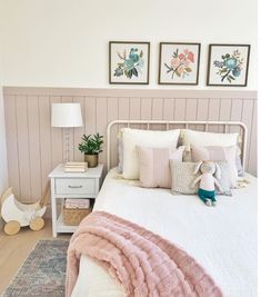 a white bed topped with pillows next to two framed pictures on the wall above it