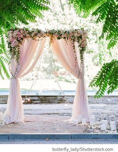 an outdoor wedding ceremony setup with pink drapes and flowers on the altar, surrounded by greenery