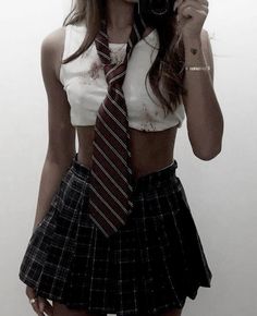 a young woman wearing a skirt and shirt with a tie around her neck holding a camera