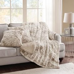 a couch with a blanket on it next to a table and lamp in front of a window